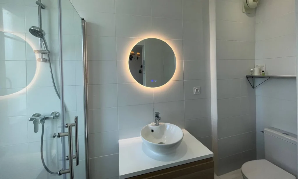Modern bathroom with glass shower, illuminated mirror and designer sink. Clean and functional decoration.