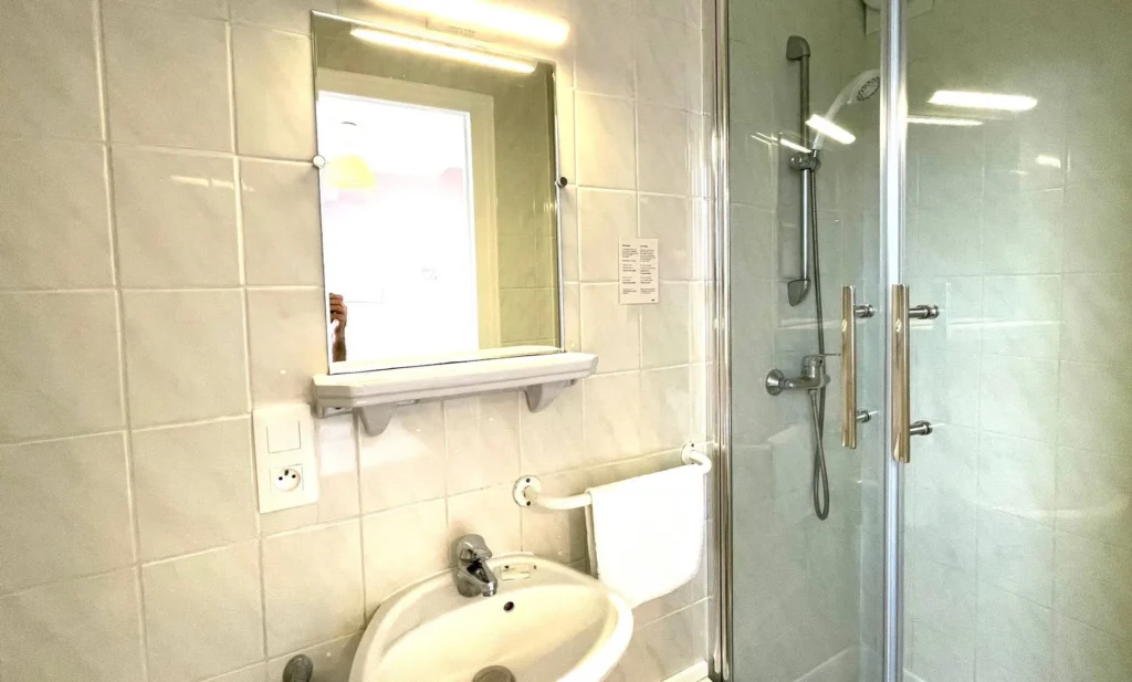 Modern bathroom with shower, sink and mirror, decorated with light tiles.